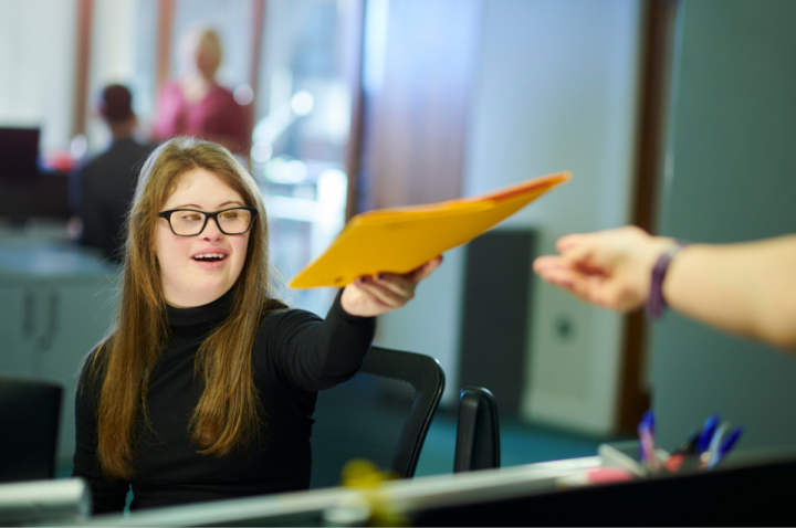 Young woman hands a folder to a coworker.